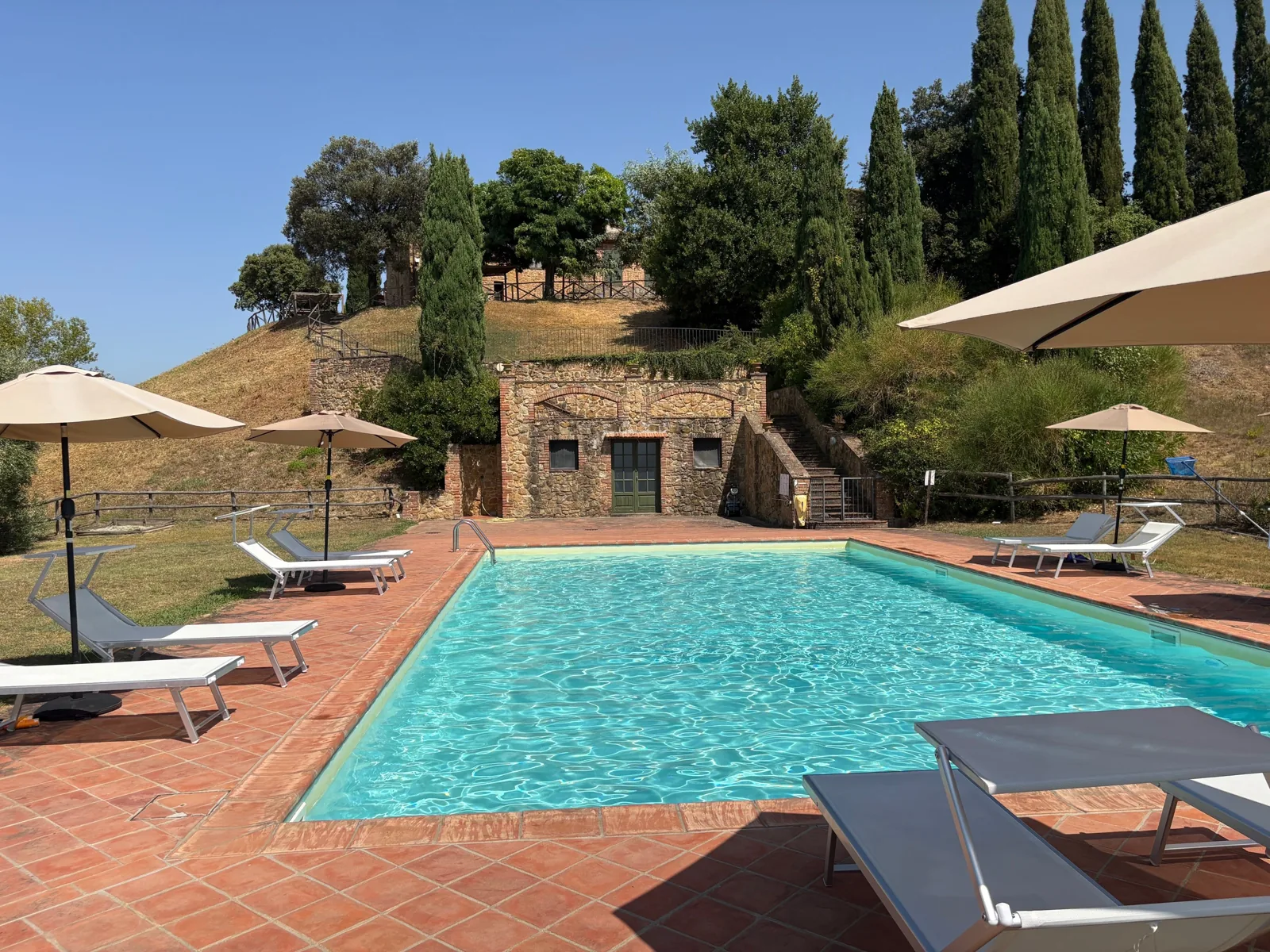 Sunlit swimming pool surrounded by cypress trees in Tuscany